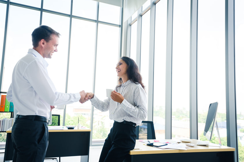 Laughing woman shaking hands with adult site broker in well-lit office
