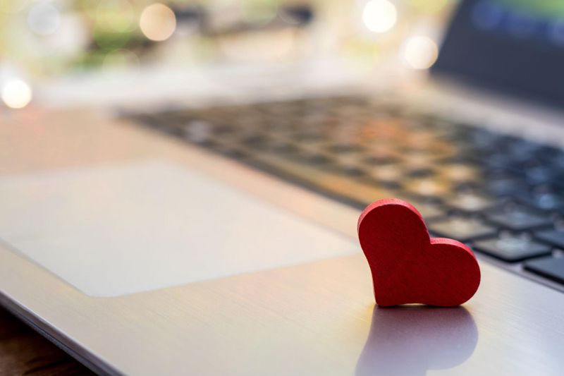 Small wooden heart resting on laptop open to online dating site