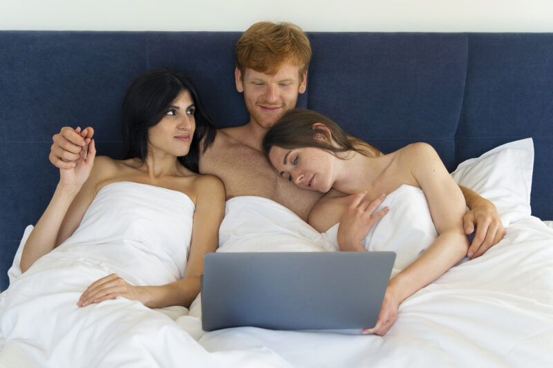polyamorous-couple-home-bed-with-laptop