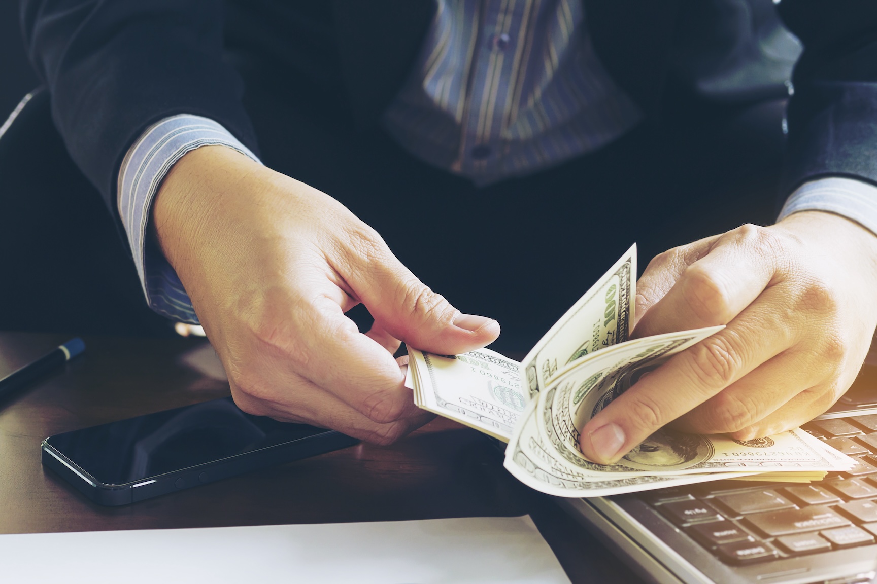 Man counting hundred dollar bills near a keyboard