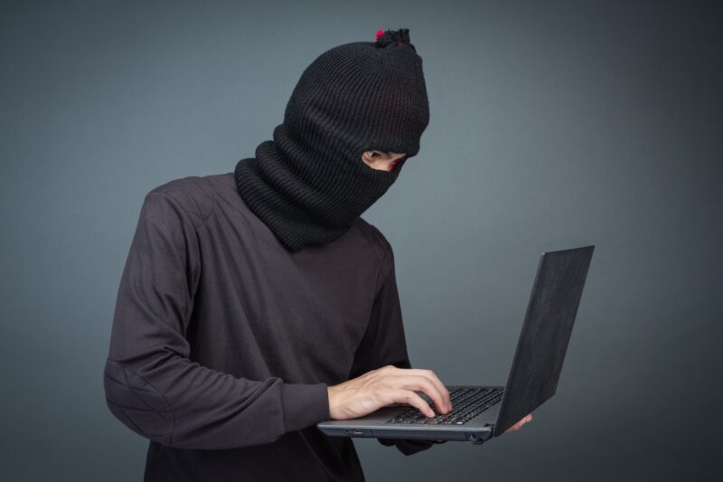 A man in a black hood holding a laptop