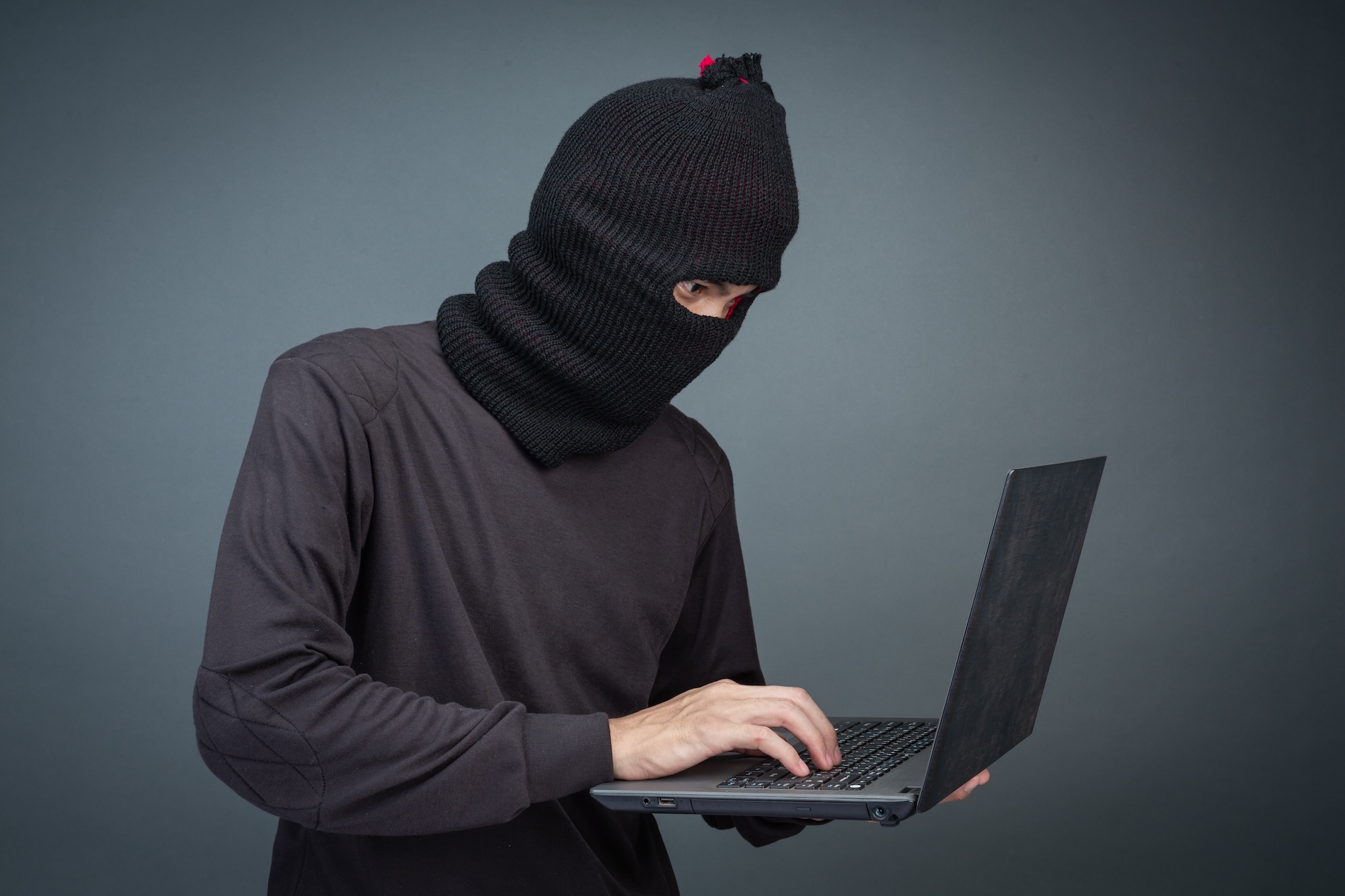 A man in a black hood holding a laptop