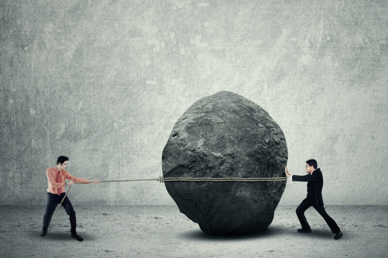 Two men in a tug of war with a rock